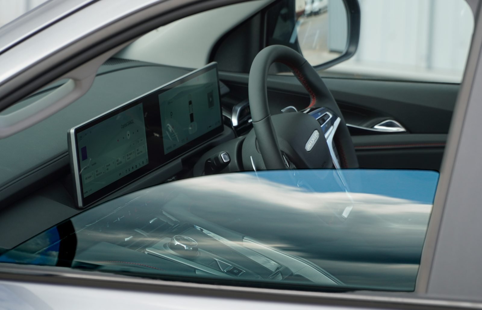 Inside the Maxus T60 cab showing the dual widescreen displays, leather steering wheel with red stitching and the 8 speed automatic in Park